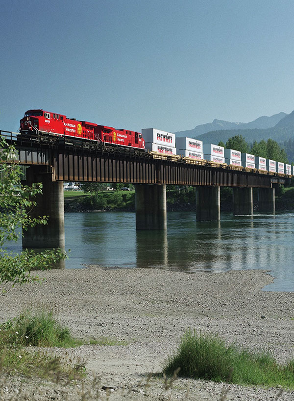 Un train du CP qui traverse un pont et transporte plusieurs conteneurs de marchandises Fastfrate